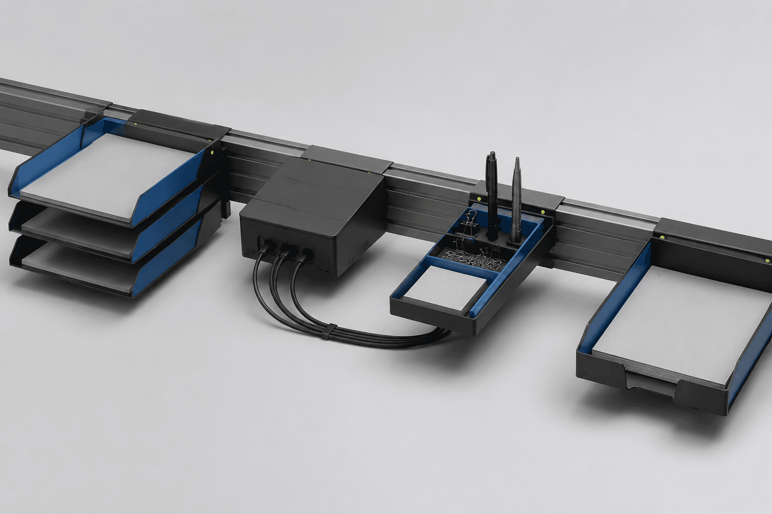 A modular desk dock system on one rail: document trays, a cable box and a pen tray under cool studio light